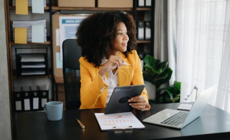 Téléchargez les photos : Belle femme d'affaires africaine avec ordinateur portable et tablette au bureau moderne - en image libre de droit
