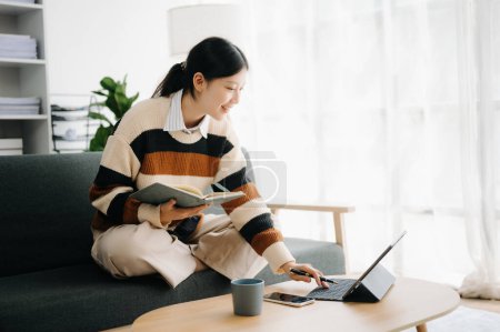 Téléchargez les photos : Femme asiatique confiante avec bloc-notes et tablette PC dans le salon sur le canapé au bureau à la maison - en image libre de droit