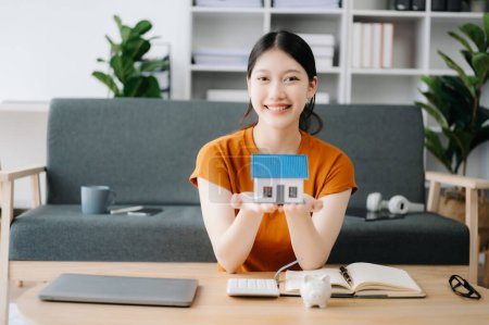 Téléchargez les photos : Asiatique Jeune agent immobilier travailleur travaillant avec ordinateur portable dans le bureau et la petite maison - en image libre de droit