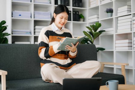 Téléchargez les photos : Femme asiatique confiante avec bloc-notes dans le salon sur le canapé au bureau à la maison - en image libre de droit