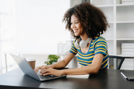 Téléchargez les photos : Étudiante, fille africaine assise au bureau à l'aide d'un ordinateur portable - en image libre de droit