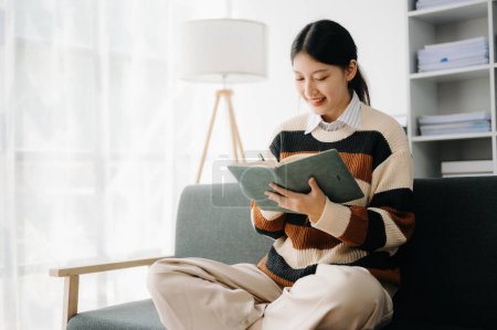 Téléchargez les photos : Femme asiatique confiante avec bloc-notes dans le salon sur le canapé au bureau à la maison - en image libre de droit
