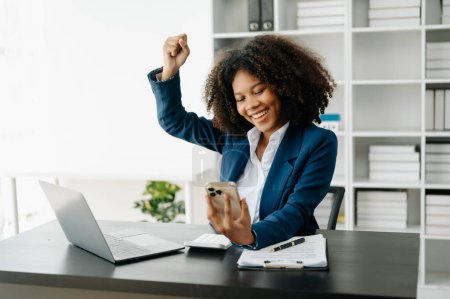 Téléchargez les photos : Femme d'affaires africaine ravie et heureuse avec ordinateur portable au bureau. - en image libre de droit