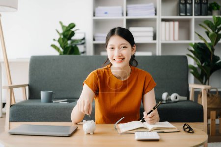 Foto de Mujer asiática y alcancía sobre la mesa para negocios, finanzas, ahorro de dinero y concepto de inversión inmobiliaria - Imagen libre de derechos