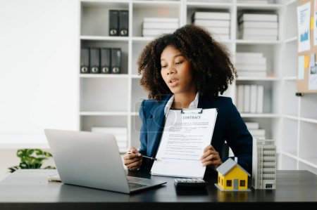 Téléchargez les photos : Jeune agent immobilier travailleur travaillant avec ordinateur portable à la table dans un bureau moderne - en image libre de droit