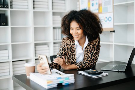 Photo for Young African woman with phone and laptop  working at modern office - Royalty Free Image