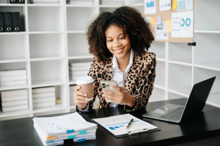 Téléchargez les photos : Femme d'affaires utilisant ordinateur portable et téléphone avec café dans le bureau moderne - en image libre de droit