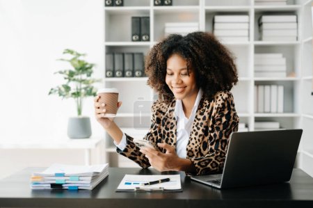 Téléchargez les photos : Femme d'affaires utilisant ordinateur portable et téléphone avec café dans le bureau moderne - en image libre de droit