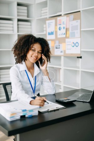 Téléchargez les photos : Femme d'affaires utilisant un ordinateur portable et un téléphone dans un bureau moderne - en image libre de droit