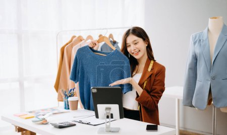 Photo for Asian influencer woman promoting and selling clothes during video call on digital tablet - Royalty Free Image