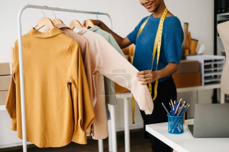 Téléchargez les photos : Image recadrée de la couturière afro-américaine travaillant dans la salle d'exposition de vêtements, vérifier la qualité des vêtements - en image libre de droit