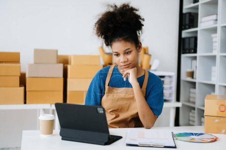 Téléchargez les photos : Femme afro-américaine travaillant au bureau avec tablette numérique, pensant tout en regardant l'écran, main sur le menton - en image libre de droit