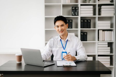 Téléchargez les photos : Jeune homme d'affaires asiatique travaillant avec des documents dans un bureau moderne. Fiscalité, rapport, comptabilité, statistiques et recherche analytique concept - en image libre de droit