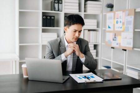 Téléchargez les photos : Frustré jeune homme d'affaires travaillant sur ordinateur portable assis sur son lieu de travail dans un bureau moderne - en image libre de droit