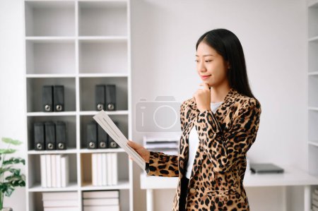 Foto de Joven atractivo Asiática mujer oficina trabajador trajes de negocios sonriendo a la cámara con el bloc de notas de trabajo, tabletas y portátiles documentos - Imagen libre de derechos