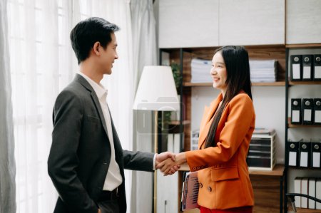 Foto de Un apretón de manos de hombre de negocios con la empresaria asiática en la oficina. Ejecutivos celebrando el éxito de la empresa - Imagen libre de derechos