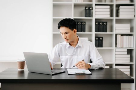 Téléchargez les photos : Jeune homme d'affaires asiatique travaillant avec des documents dans un bureau moderne. Fiscalité, rapport, comptabilité, statistiques et recherche analytique concept - en image libre de droit