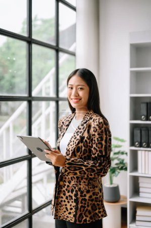 Photo for Young attractive Asian female office worker business suits smiling at camera with working notepad, tablet and laptop documents - Royalty Free Image