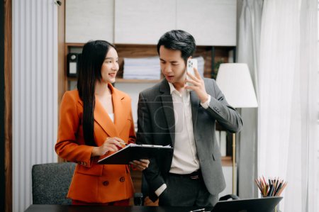 Foto de Dos empresarios asiáticos discuten proyecto de inversión de trabajo y la estrategia de planificación con el teléfono en la oficina moderna. - Imagen libre de derechos