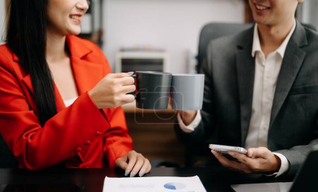 Téléchargez les photos : Deux travailleurs d'affaires asiatiques assis et tenant une tasse de café dans un bureau moderne, réussi, célébration, nouveau projet, concept de bureau d'équipe le matin - en image libre de droit