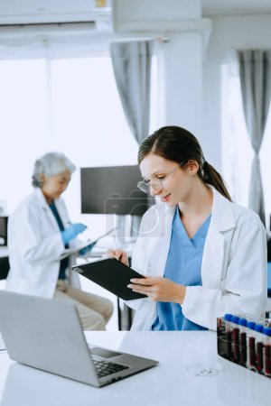 Photo for Two scientist or medical technician working, having a medical discuss meeting with an Asian senior female scientist supervisor in the laboratory with online reading, test samples - Royalty Free Image