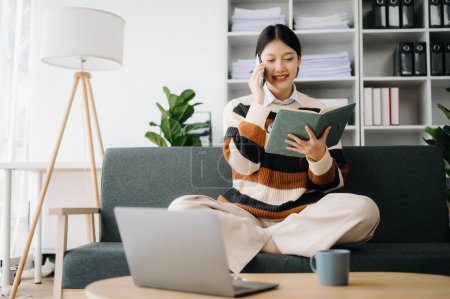 Téléchargez les photos : Confiant asiatique femme lecture livre dans le salon sur le canapé au bureau à domicile - en image libre de droit