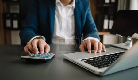 Photo for Women counting coins on calculator taking from the piggy bank. hand holding pen working on calculator to calculate on desk about cost at office - Royalty Free Image