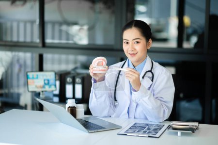 Photo for Concentrated dentist sitting at table with jaw samples tooth model and working with tablet and laptop in dental office professional dental clinic. medical doctor working - Royalty Free Image