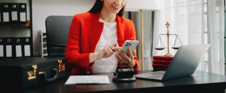 Photo for Cropped image of  lawyer woman wearing red jacket, working at office desk with laptop and using mobile, - Royalty Free Image