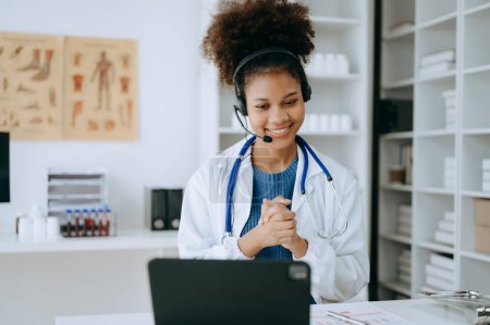 Photo for Attractive African female doctor talking while explaining medical treatment to patient through a video call with laptop in office - Royalty Free Image