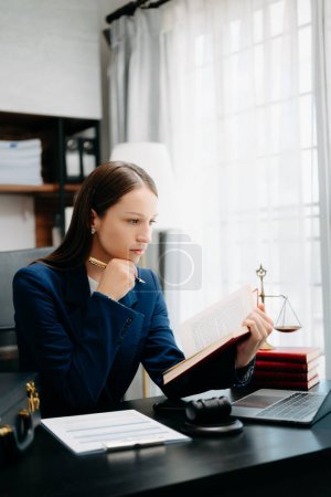 Téléchargez les photos : Femme caucasienne lecture livre de justice avec travail dans le bureau à la table avec ordinateur portable - en image libre de droit
