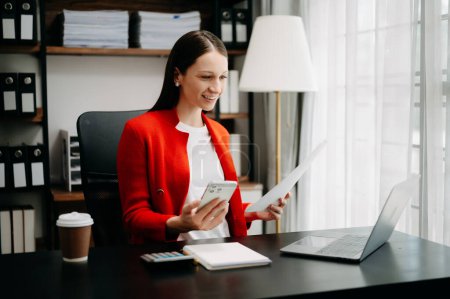 Téléchargez les photos : Expert d'affaires confiant attrayant souriant jeune femme caucasienne tapant ordinateur portable ang tenant tablette numérique sur le bureau dans le bureau créatif - en image libre de droit