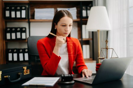 Photo for Caucasian lawyer woman wearing red jacket, working at office desk with laptop - Royalty Free Image