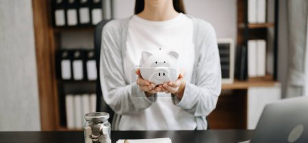 Photo for Cropped image of woman holding piggy bank, table with coins, laptop and notebook - Royalty Free Image