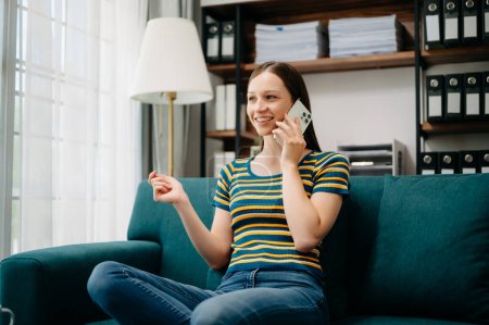 Foto de Sonriente mujer caucásica hablando en el teléfono móvil mientras está sentado en el sofá en la sala de estar - Imagen libre de derechos