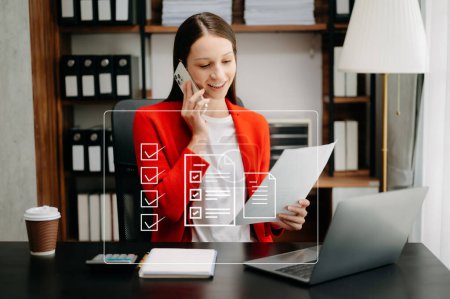 Téléchargez les photos : Femme d'affaires caucasienne portant une veste rouge, travaillant au bureau avec ordinateur portable et utilisant un téléphone mobile, - en image libre de droit
