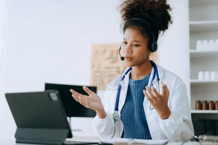 Photo for Attractive African female doctor talking while explaining medical treatment to patient through a video call with laptop in office - Royalty Free Image