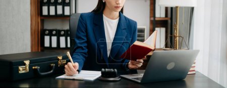 Téléchargez les photos : Image recadrée de femme caucasienne écrivant des notes, lecture livre de justice avec travail dans le bureau à table avec ordinateur portable - en image libre de droit