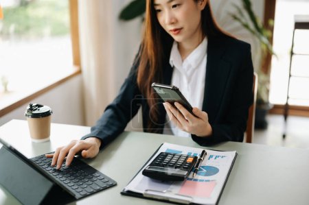 Téléchargez les photos : Asiatique Femme d'affaires travaillant dans un bureau bancaire avec tablette numérique et tenant un téléphone mobile - en image libre de droit