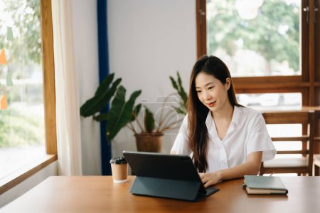 Téléchargez les photos : Asiatique femme d'affaires travaillant avec tablette PC et boire du café dans le bureau moderne - en image libre de droit