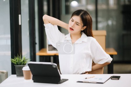 Téléchargez les photos : Jeune femme d'affaires asiatique surmenée souffrant de douleurs au cou après une longue journée à son bureau. concept de syndrome de bureau - en image libre de droit
