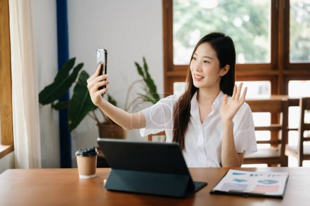 Photo for Asian businesswoman working working with tablet pc and talking over mobile phone in modern office - Royalty Free Image