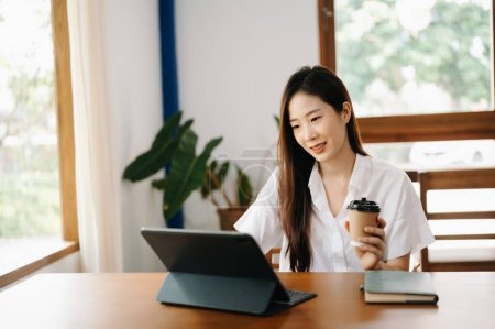 Téléchargez les photos : Asiatique femme d'affaires travaillant avec tablette PC et boire du café dans le bureau moderne - en image libre de droit