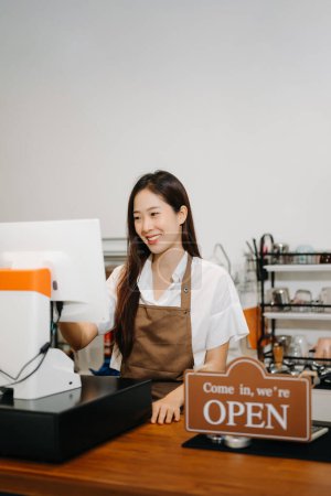 Foto de Dueño de una pequeña empresa. Mujer asiática trabajando en el mostrador en la cafetería. Mujer camarera, propietaria de coffeeshop. - Imagen libre de derechos