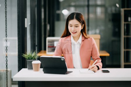 Téléchargez les photos : Jeune belle femme asiatique tapant sur ordinateur portable tout en étant assis au bureau de la table blanche de travail - en image libre de droit