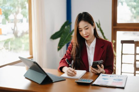 Foto de Mujer de negocios asiática que trabaja en la oficina en la mesa del lugar de trabajo con el ordenador portátil, notas de escritura, documentos de factura, cálculo de finanzas - Imagen libre de derechos