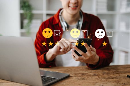 Téléchargez les photos : Concept d'évaluation du service client. Asiatique homme d'affaires pressant visage sourire émoticône sur écran virtuel dans le bureau - en image libre de droit