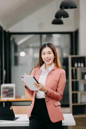 Téléchargez les photos : Femme asiatique confiante avec un sourire travaillant sur tablette numérique dans un bureau moderne - en image libre de droit