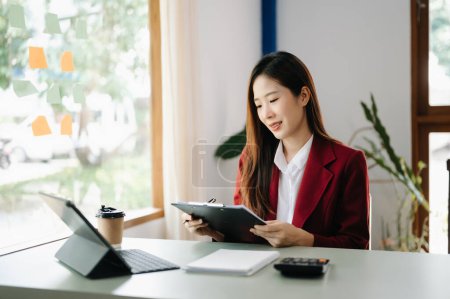 Téléchargez les photos : Asiatique Femme d'affaires travaillant dans le bureau à la table de travail avec ordinateur portable, tenant dossier avec les documents de facture, le calcul des finances - en image libre de droit