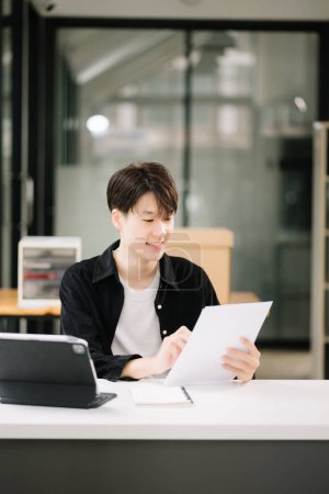 Foto de Joven atractivo hombre asiático trabajando con sus notas en la oficina moderna - Imagen libre de derechos